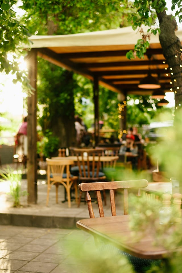 Die begrünte Pergola-Terrasse mit hellen Holzstühlen im Sommerlicht.